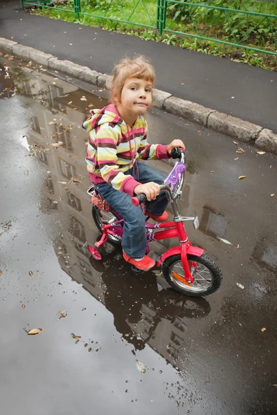 Fille va sur un vélo sur asphalte humide — Photo