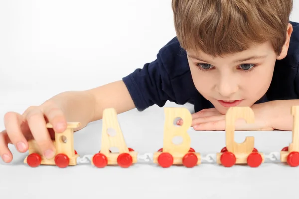 Little boy lying on floor and playing with wooden alphabet railw — Stock Photo, Image
