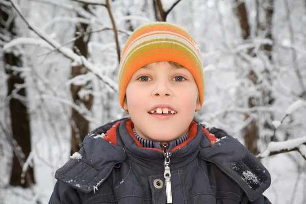 Улыбающийся мальчик в кепке зимой в лесу — стоковое фото
