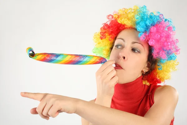 Junge Schönheitskönigin mit Clownsperücke und Party-Gebläse zeigt nach links, — Stockfoto