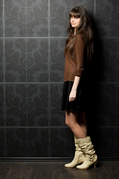 Beautiful young woman against wall with pattern, standing sidewa