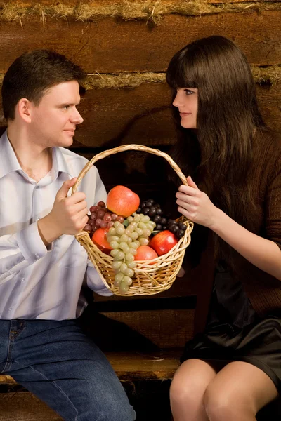 Smiling man and woman with basket of fruit sitting on bench — Stock Photo, Image