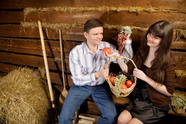 Smiling man and woman with basket of fruit sitting on bench — Stock Photo, Image