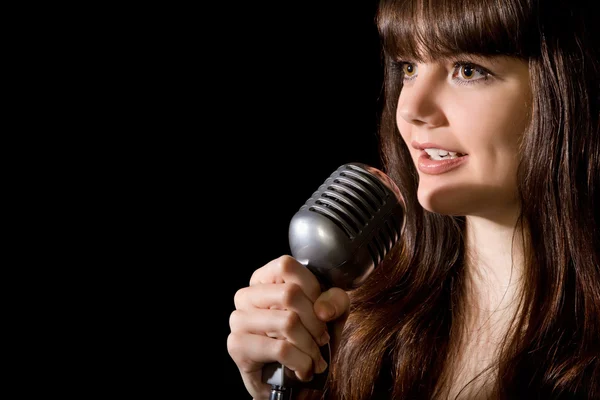 Mladá krásná žena zpívat do mikrofonu izolovaných na černém pozadí — Stock fotografie