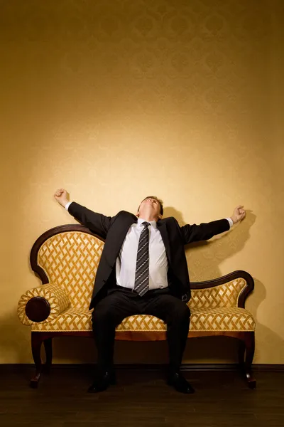 Бизнесмен в костюме тянется после сна, сидя на диване — стоковое фото