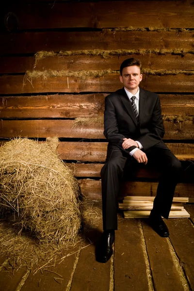 Homme d'affaires assis sur un banc près d'une botte de foin dans une cabane en bois — Photo