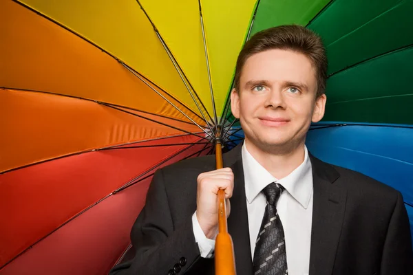 Smiling businessman in suit with multi-coloured umbrella — Stock Photo, Image