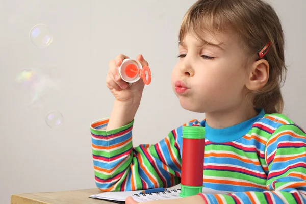 Маленька біла дівчинка в різнокольоровій сорочці дме мильні бульбашки — стокове фото