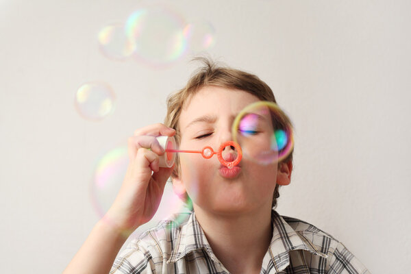 Little caucasian boy blowing soap bubbles on white background, f