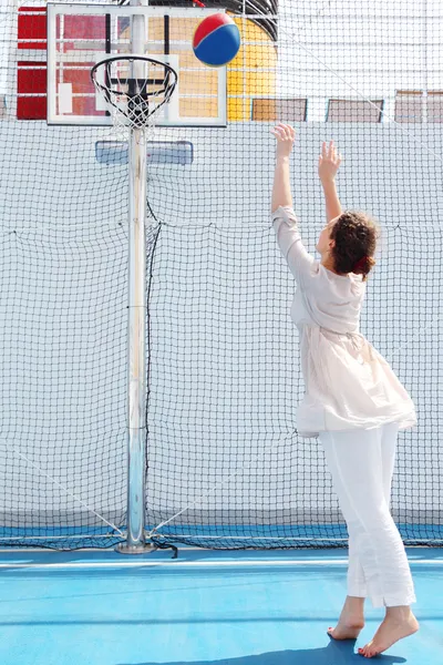 Bruneta žena v bílých šatech hází míč v koši, pohled od b — Stock fotografie