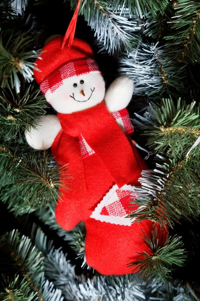 Muñeco de nieve de juguete sonriente en ropa roja colgando de un árbol de piel de Navidad —  Fotos de Stock