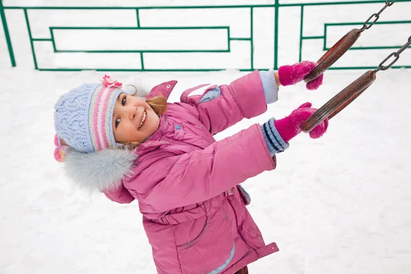 Vrij lachende meisje in roze jas op speelplaats in winte — Stockfoto