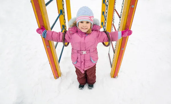Pequena menina sorridente bonita em jaqueta rosa no playground em winte — Fotografia de Stock