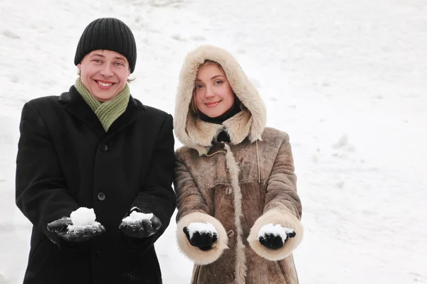 Young man and girl in warm dress smiling and holding snowballs, — Stock Photo, Image