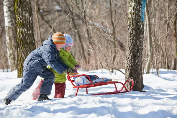 Menino e menina empurrar trenó no inverno em madeira — Fotografia de Stock