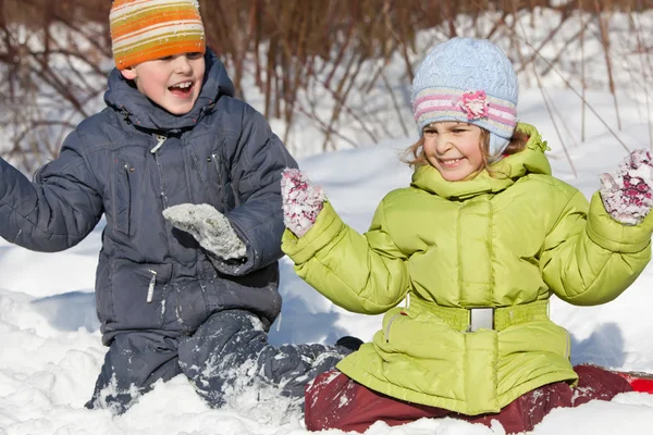 Menino e menina brincam sentados na neve no inverno em madeira — Fotografia de Stock