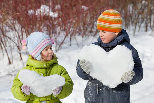 Teenager boy and little girl keeps in hands hearts from snow in — Stock Photo, Image