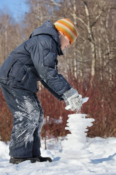 Chico crea pirámide de hielo en día soleado en invierno en madera, Un —  Fotos de Stock