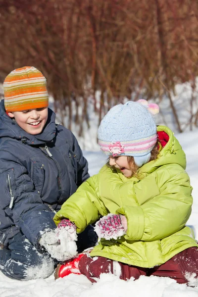 Menino e menina brincam sentados na neve no dia ensolarado no inverno — Fotografia de Stock