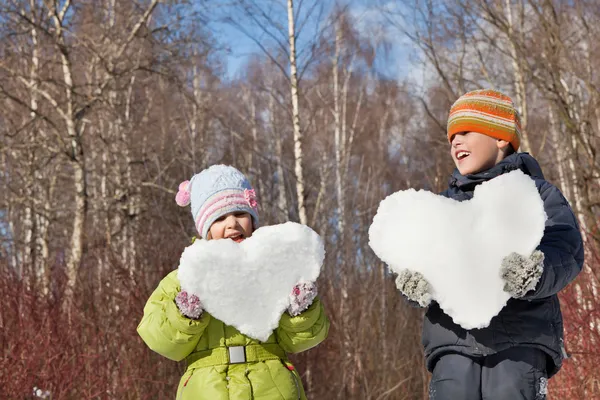 Boy and little girl keeps in hands hearts from snow in winter in — Stock Photo, Image
