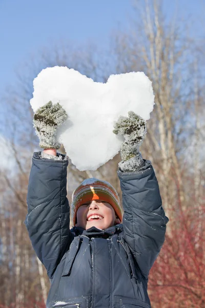 El muchacho guarda en las manos los corazones de la nieve sobre la cabeza en invierno en la madera —  Fotos de Stock