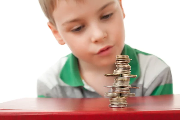 Мальчик в полосатой футболке смотрит на кривую кучу монет — стоковое фото