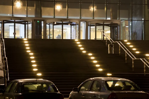 Grand entrance in modern office building at night, two cars on p