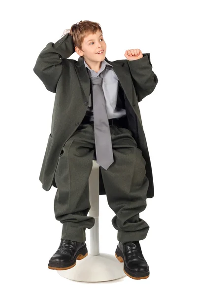 Little boy in big grey man's suit sitting on chair isolated on w — Stock Photo, Image
