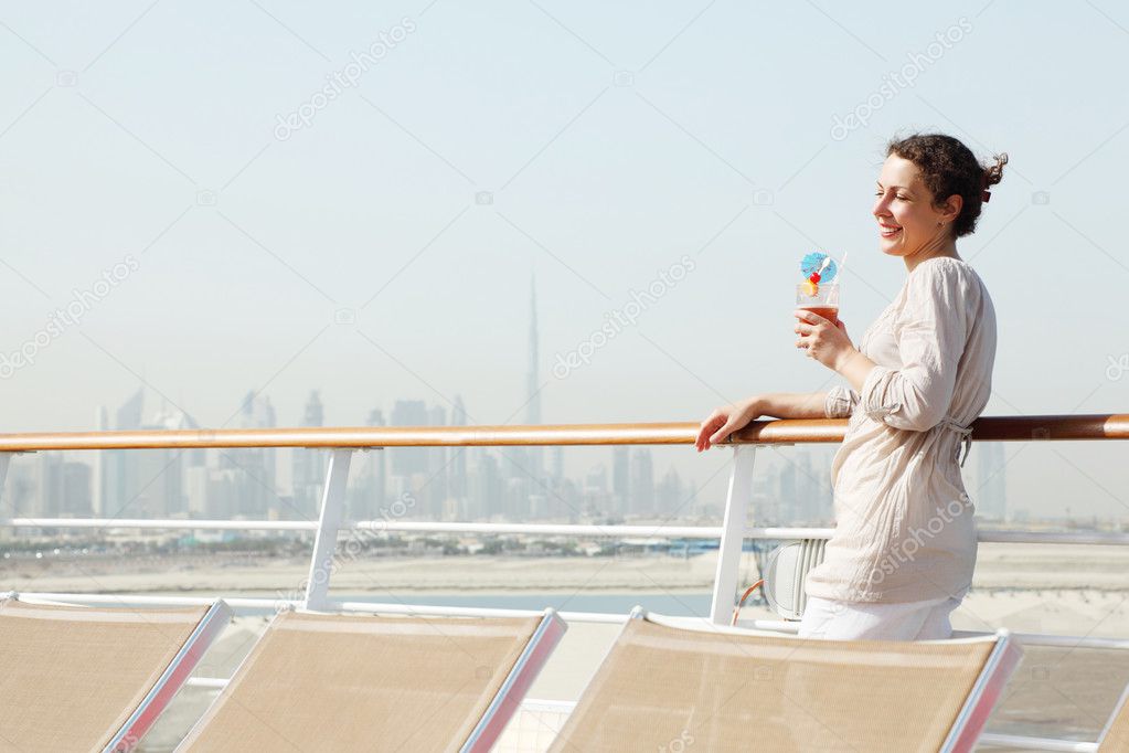 Young beauty woman with cocktail standing on cruise liner deck,