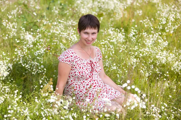 Cheerful pregnant woman sitting in chamomile — Stock Photo, Image