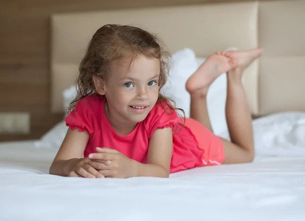 Glad liten flicka ligger på sängen. — Stockfoto
