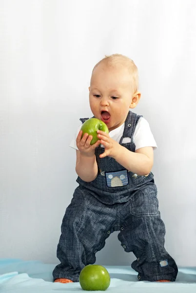 One year old kid eats a green apple. — Stock Photo, Image