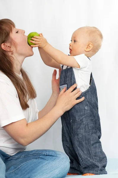 One year old baby feeds her mother an apple. — Stock Photo, Image