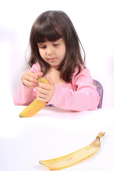 Маленькая девочка чистит банан — стоковое фото