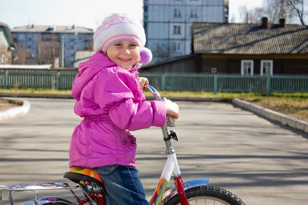 Uma menina andando de bicicleta no quintal . — Fotografia de Stock
