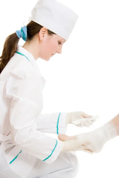 Una doctora le sacude la pierna con una venda sobre un fondo blanco . —  Fotos de Stock