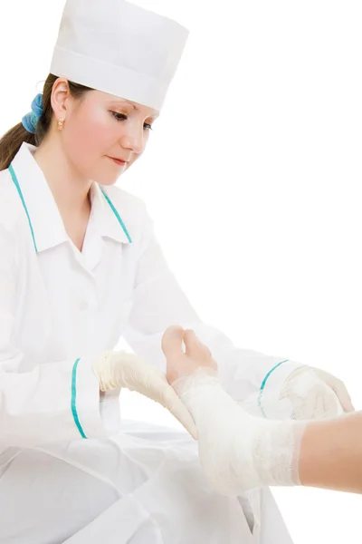 En kvinna läkare skakar benet med ett bandage på vit bakgrund. — Stockfoto