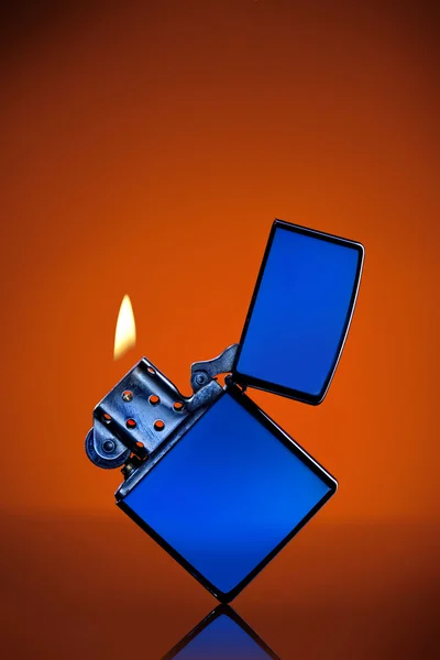 Modré zippo zapalovač s plamenem na oranžovém pozadí — Stock fotografie