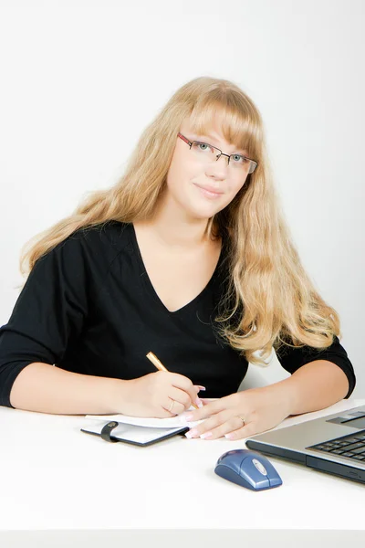 Flicka med en bärbar dator skriver i en anteckningsbok — Stockfoto