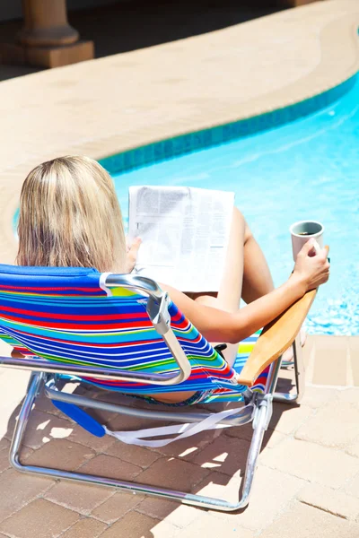 A mulher com jornal perto da piscina Imagens Royalty-Free