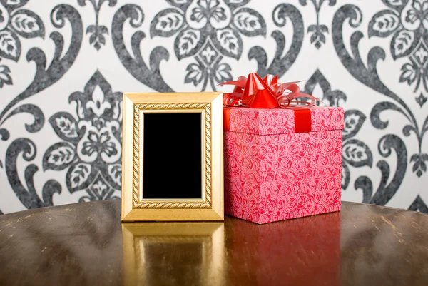 Golden photo frame and present box on table — Stock Photo, Image