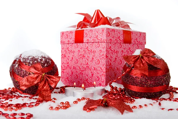 Рождественская коробка в снегу с красными шариками и свечами — стоковое фото
