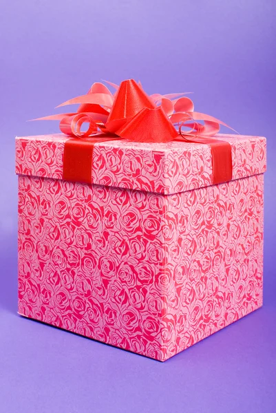 Розовая подарочная коробка с красной лентой на синем фоне . — стоковое фото