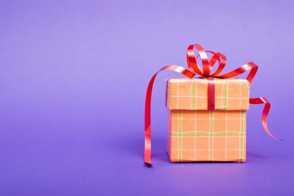 Single orange gift box with red ribbon on blue background. — Stock Photo, Image