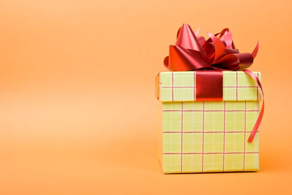 Зеленая подарочная коробка с красной лентой на желтом фоне. — стоковое фото