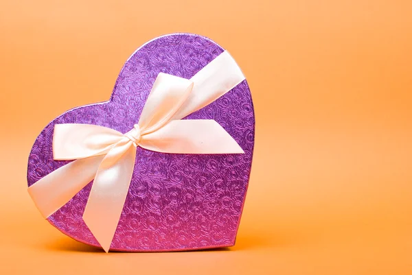 Single heart gift box with ribbon on yellow background. — Stock Photo, Image