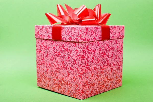 Одна розовая коробка подарка с красной лентой на зеленом фоне . — стоковое фото