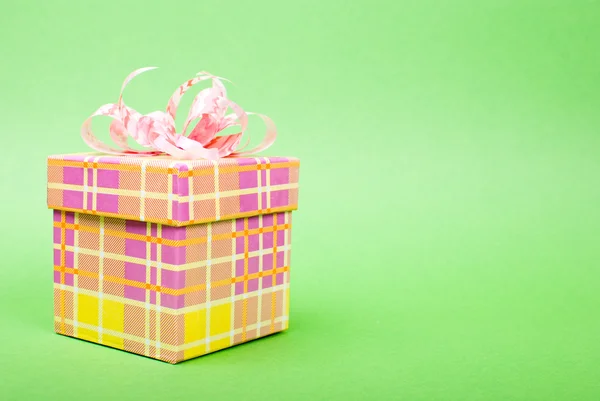 Одиночна жовта подарункова коробка з рожевою стрічкою на зеленому фоні . — стокове фото