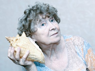 Smiling great grandmother listening to a seashell clipart