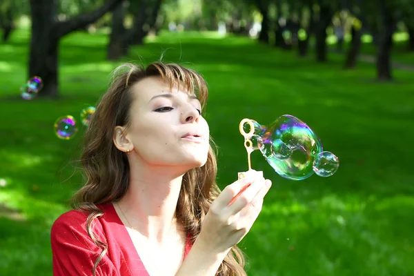 Young attractive girl inflating soap bubbles in spring park — Stock Photo, Image